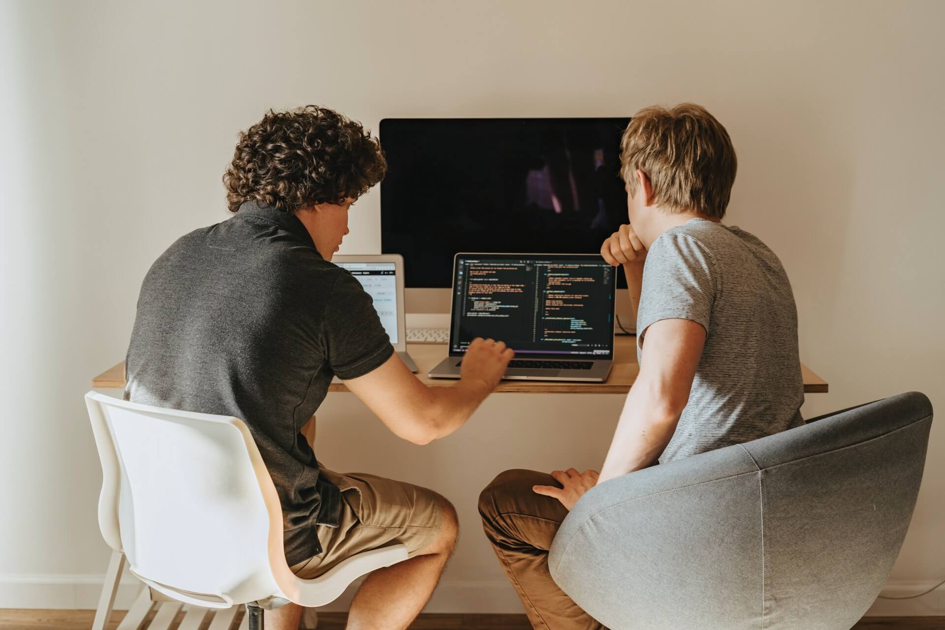 why-you-need-we-dev Two person working on their laptop working some code with a big monitor display upfront on top the table, showcasing a modern setup in web development.